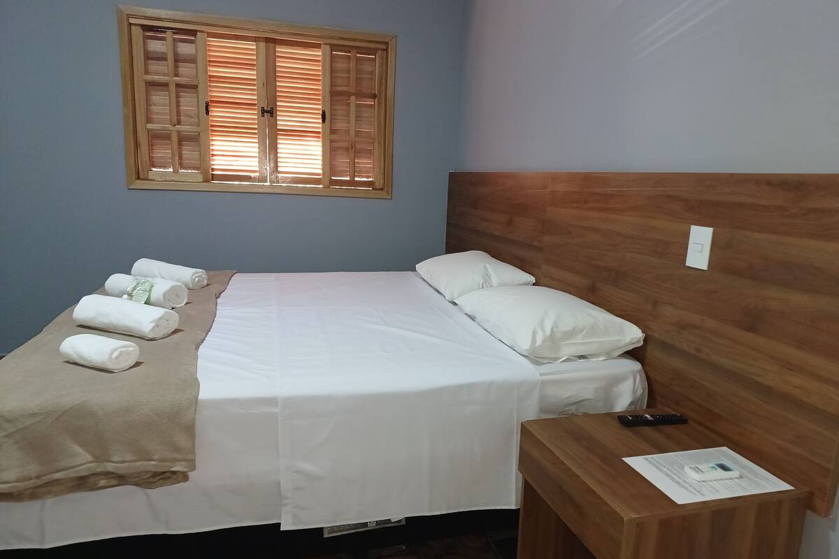 A neatly made bed with white linens, a wooden headboard, and a bedside table with a remote control and a paper.