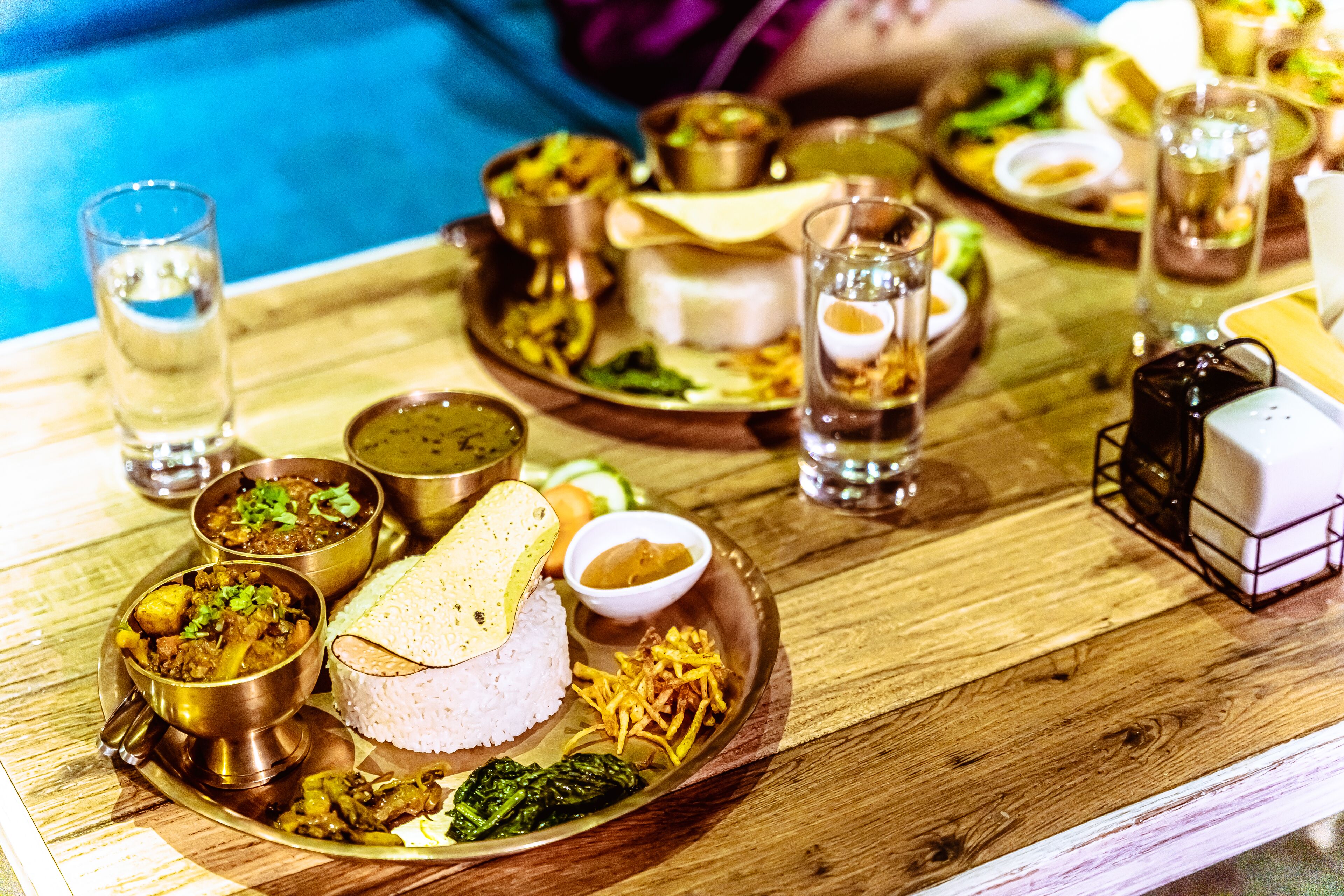 Una mesa de madera con diversos platos, como arroz, curry y pan, junto con vasos de agua.