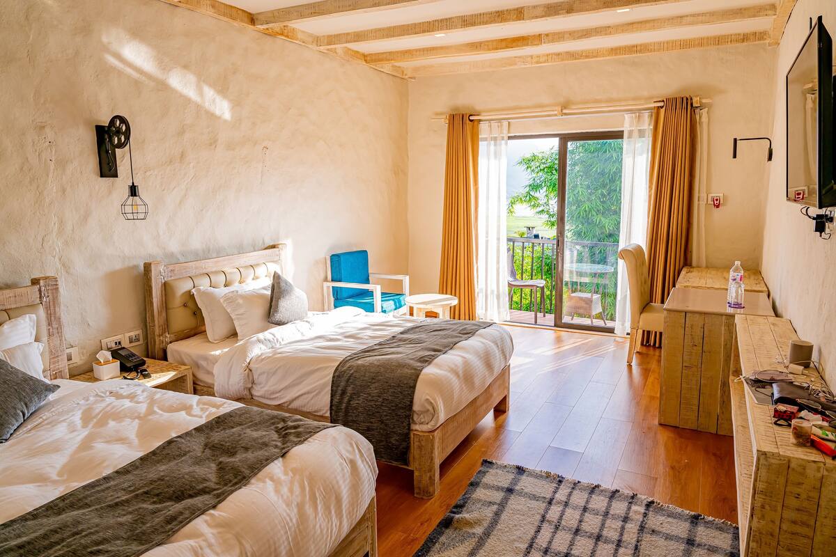 Une chambre avec deux lits, une petite table, une chaise, un bureau et une grande fenêtre avec des rideaux.