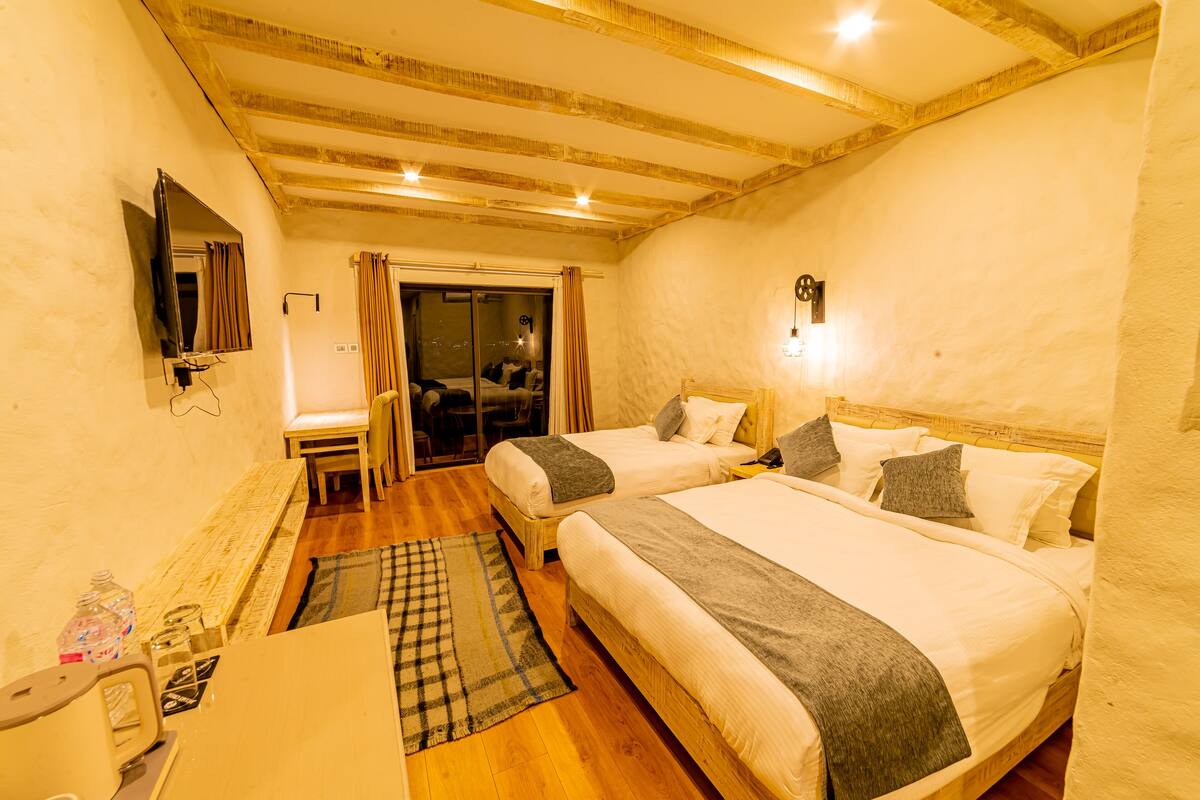 Une chambre d’hôtel avec deux lits, un bureau, une chaise, une télévision et une fenêtre avec des rideaux.
