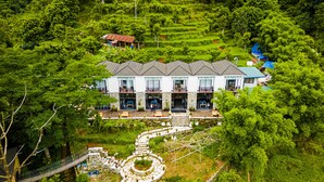 Un grand bâtiment à deux étages, doté d’une façade en pierre, de nombreux balcons et entouré d’un paysage verdoyant luxuriant.