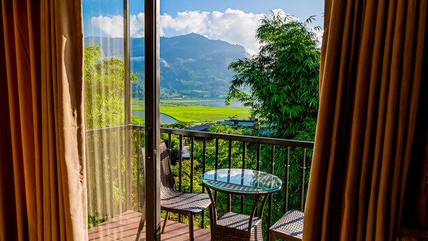 Un balcon avec une porte vitrée, une table ronde en verre et deux chaises en osier.