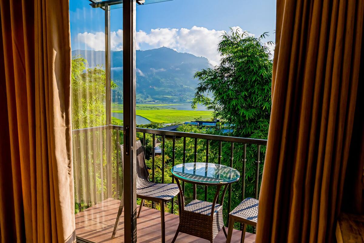 Un balcon avec une porte vitrée, une table ronde en verre et deux chaises en osier.