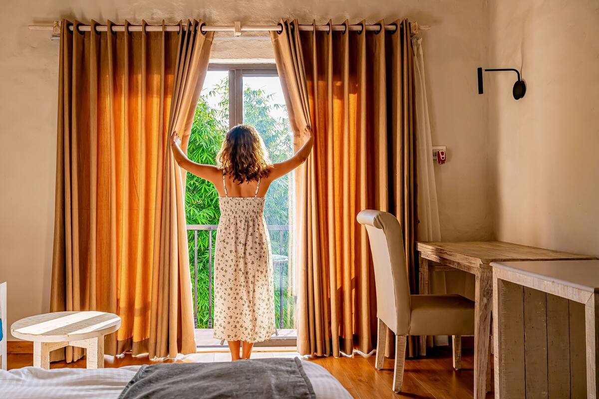 Une pièce comprenant un lit, un bureau, une chaise et une fenêtre avec des rideaux.