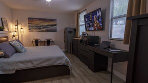 Ein Schlafzimmer mit einem Bett, Nachttischen, einem Schreibtisch mit einem Laptop, einem Kühlschrank und einem Fernseher.
