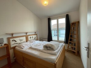Une chambre à coucher avec un lit en bois, une table de chevet, une lampe, une fenêtre avec des rideaux et une échelle en bois.