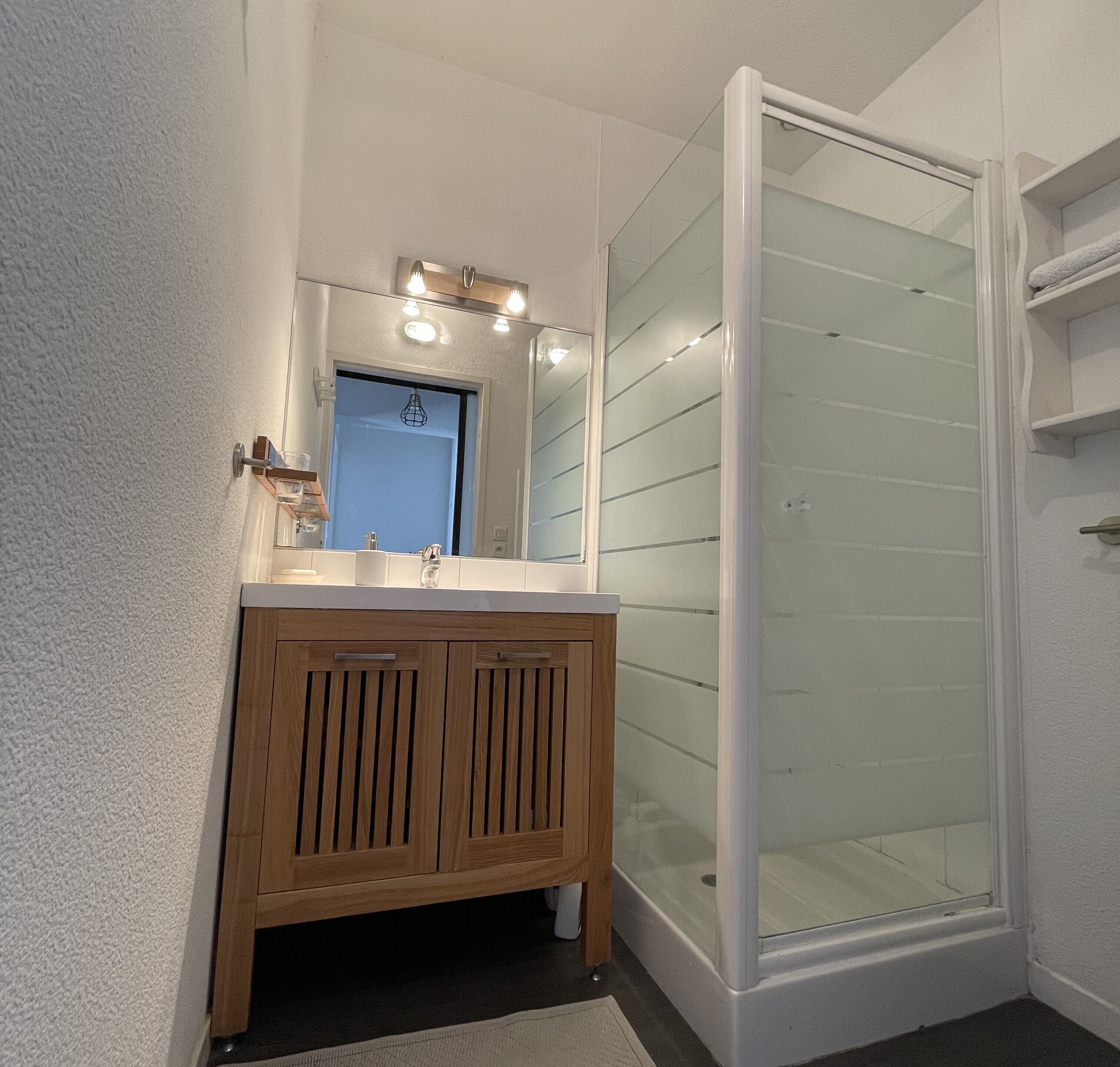 A bathroom with a wooden vanity, a mirror, and a glass shower enclosure.