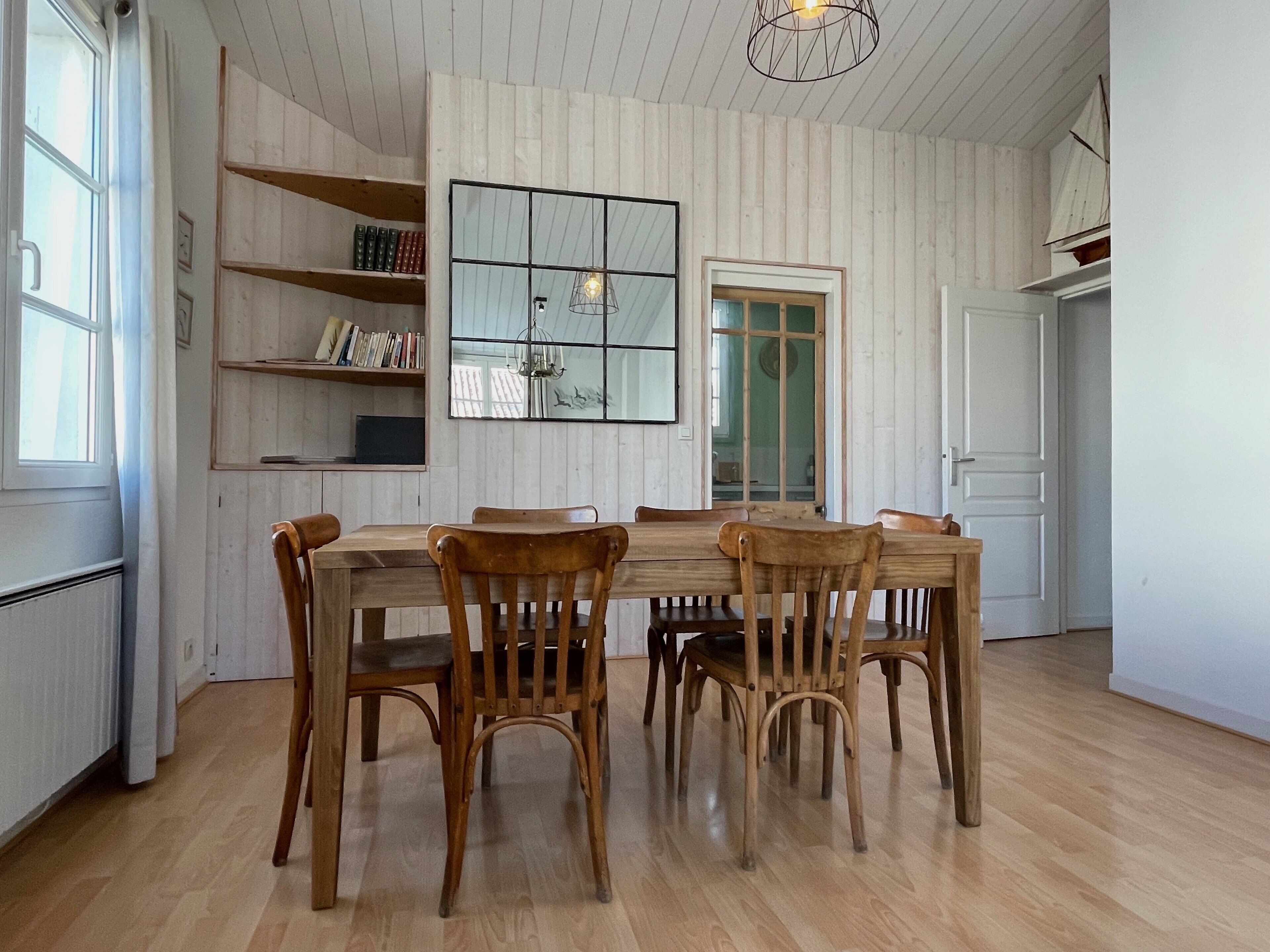 A dining area with a wooden table and chairs, a bookshelf, a mirror, and a door.