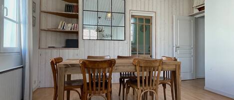 A dining area with a wooden table and chairs, a bookshelf, a mirror, and a door.