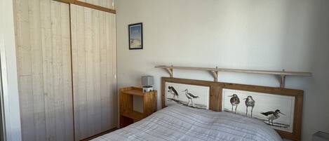 A bedroom with a bed, wooden wardrobe, framed artwork, and a nightstand.