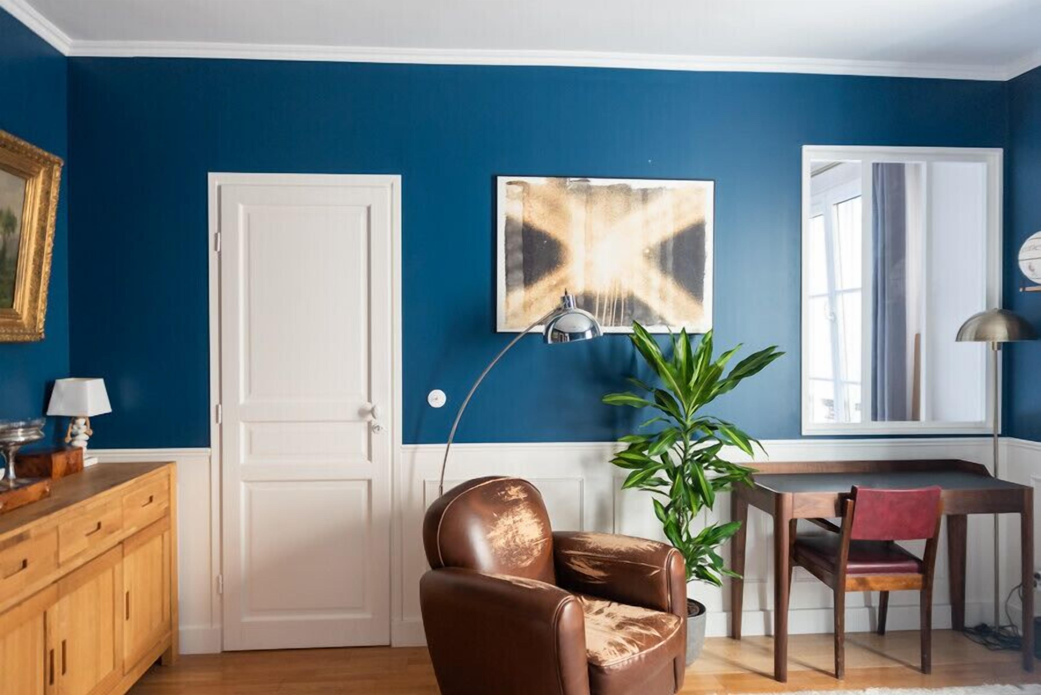 A room with a blue wall, a white door, a brown leather chair, a wooden desk, and a green plant.