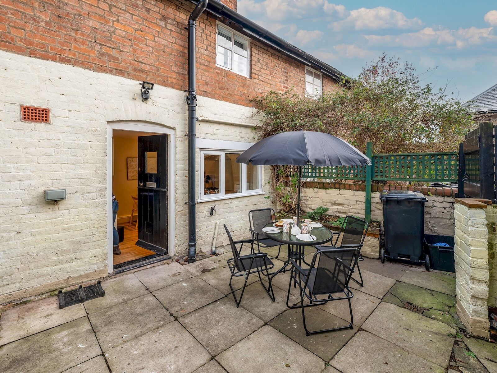 A patio with a table and chairs, a black umbrella, and a brick wall.