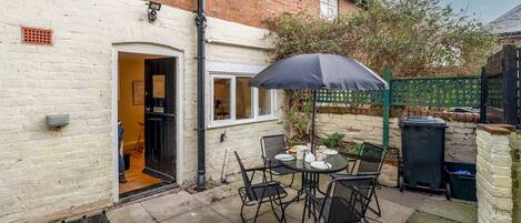 A patio with a table and chairs, a black umbrella, and a brick wall.