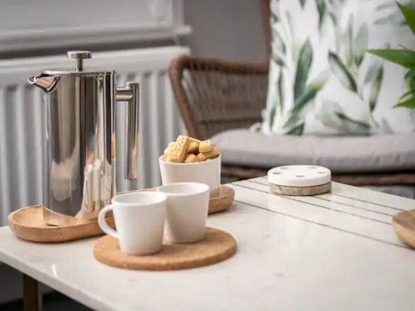 Une table avec une cafetière, deux tasses blanches, un bol de biscuits et une assiette décorative.