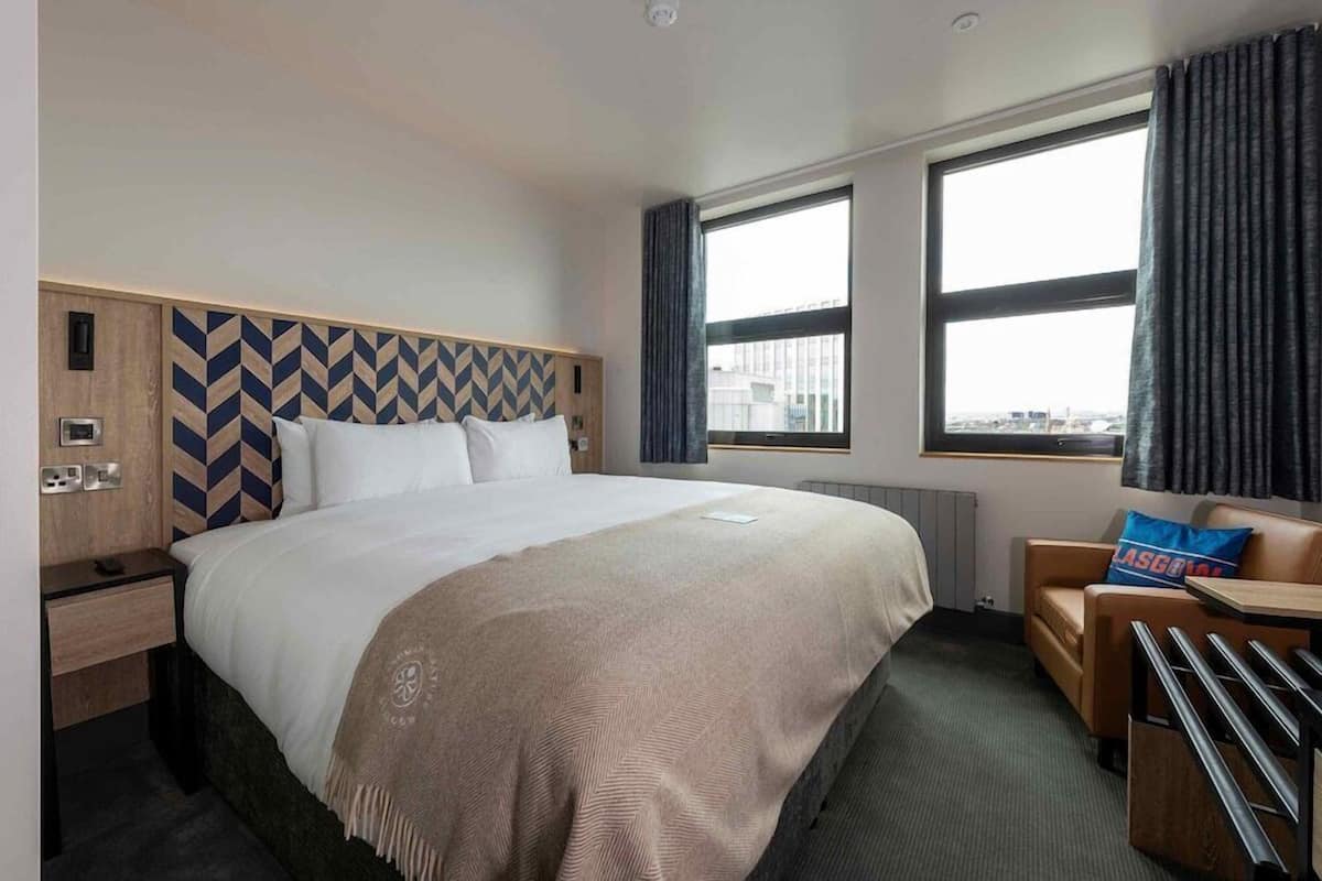 A hotel room with a large bed, a desk, a chair, and a window with curtains.