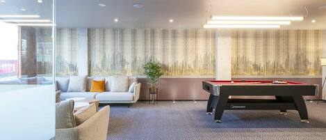 Una habitación moderna con mesa de billar, sofá y un amplio ventanal con vistas a la ciudad.