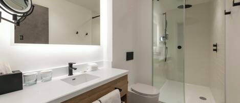Un baño moderno con ducha acristalada, un espejo grande y un tocador de madera.