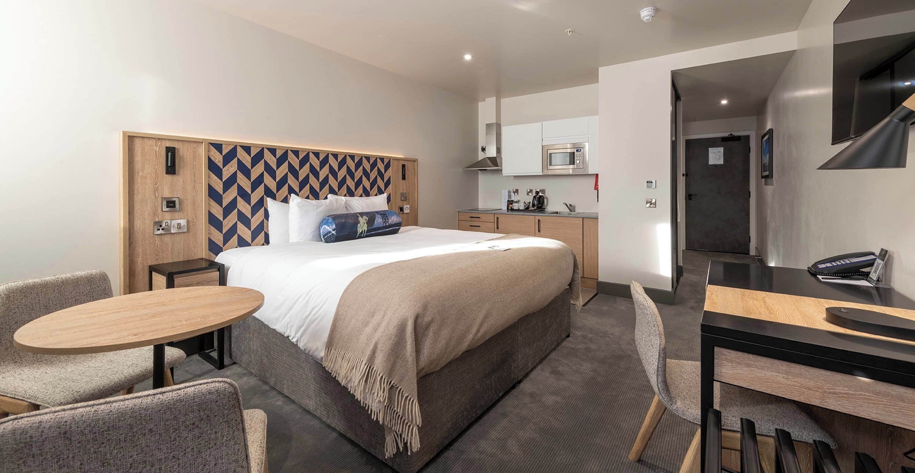 Una habitación de hotel con cama, un escritorio pequeño, una silla, una mesa y una kitchenette.