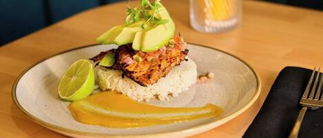 A plate with grilled chicken, avocado, and rice, accompanied by a lime wedge and a glass of orange juice.