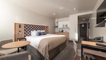 A modern hotel room with a large bed, a desk, and a kitchenette.