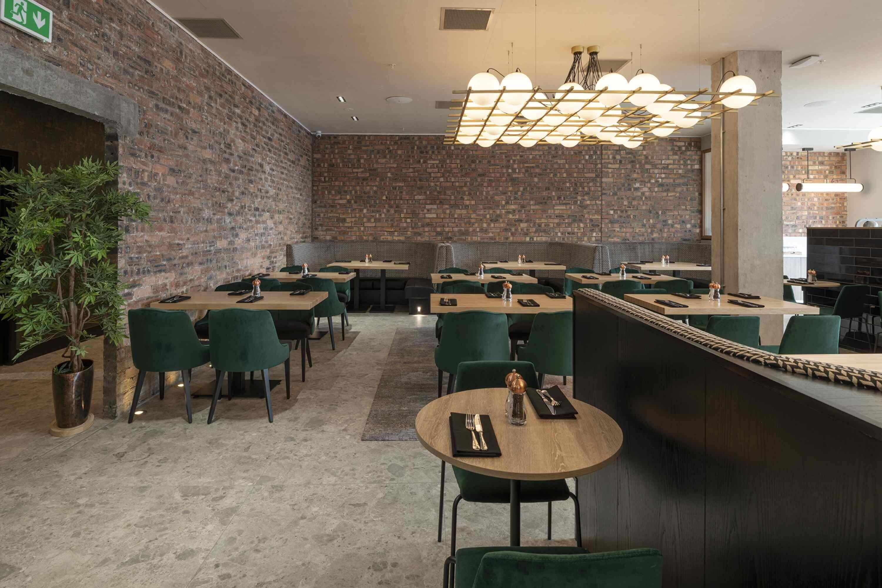 A modern restaurant with brick walls, green chairs, and a central bar area.