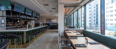 A modern bar area with multiple screens, seating, and a view of the city.