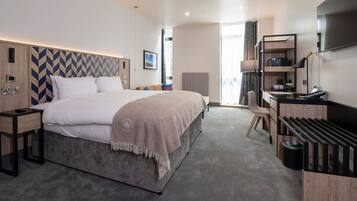 Quarto de hotel moderno com uma cama grande, escrivaninha, televisão e minibar.