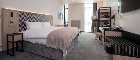 Una habitación de hotel moderna con una cama grande, un escritorio, un televisor y un mini bar.