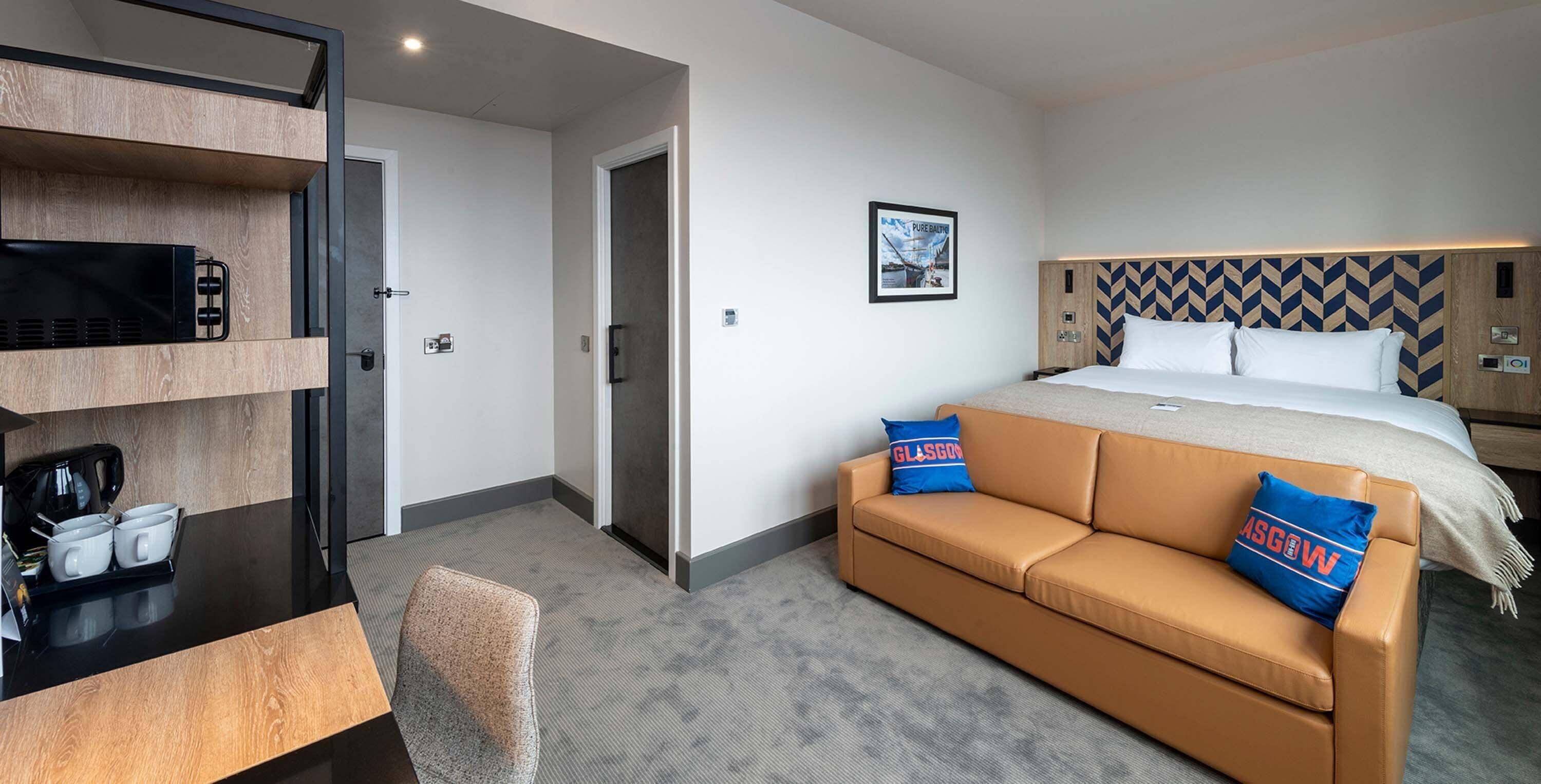 Een hotelkamer met een bed, een slaapbank, een bureau met een koffiezetapparaat, en een schilderij aan de muur.