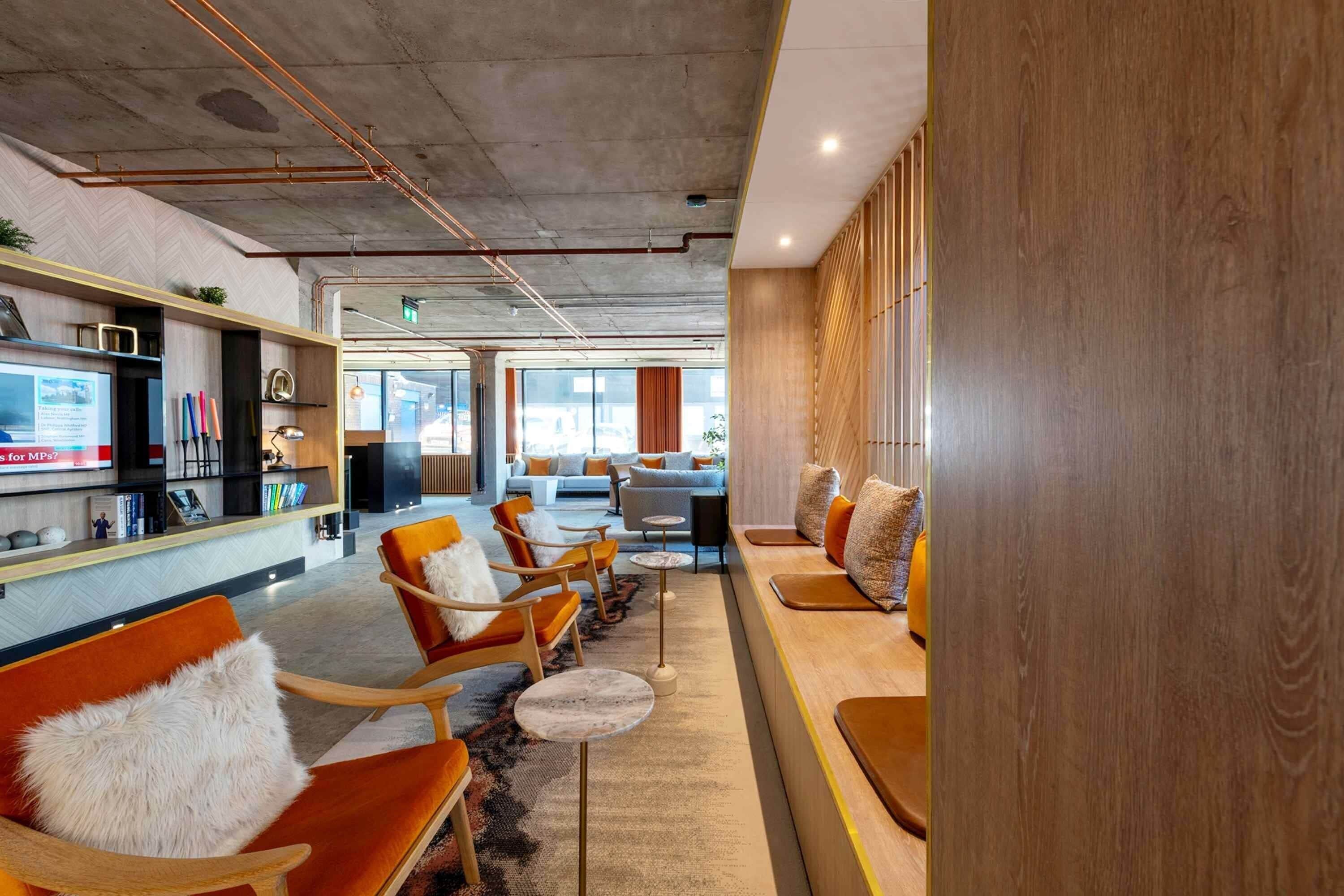 A modern lounge area with orange chairs, a wooden reception desk, and a view of the cityscape through large windows.