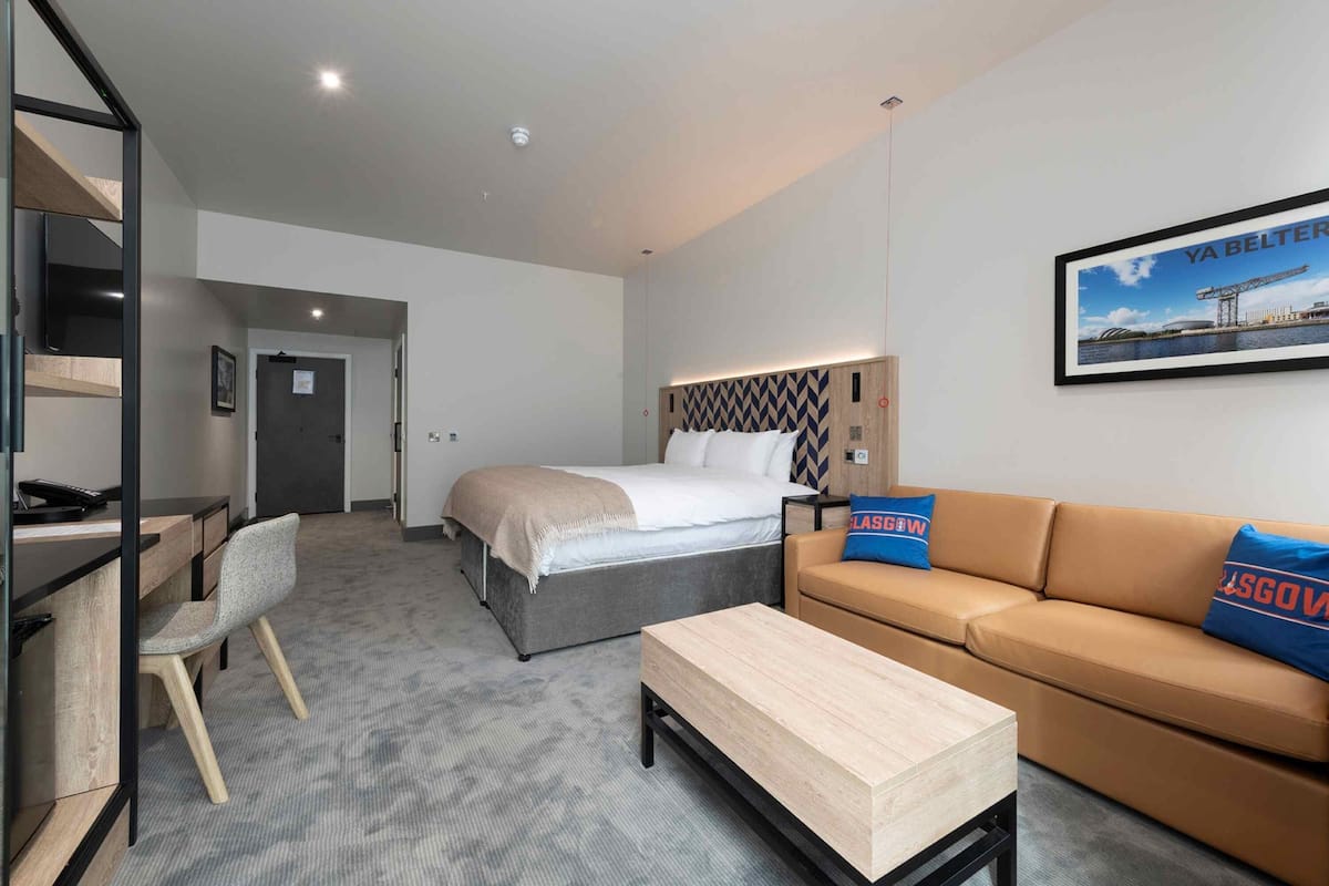 A modern hotel room with a bed, a sofa, a desk, and a chair.