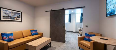 A modern hotel room with a sofa set, a coffee table, and a small dining table.