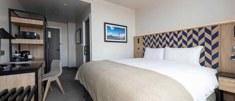 A hotel room with a bed, a desk, a chair, and a kitchenette.