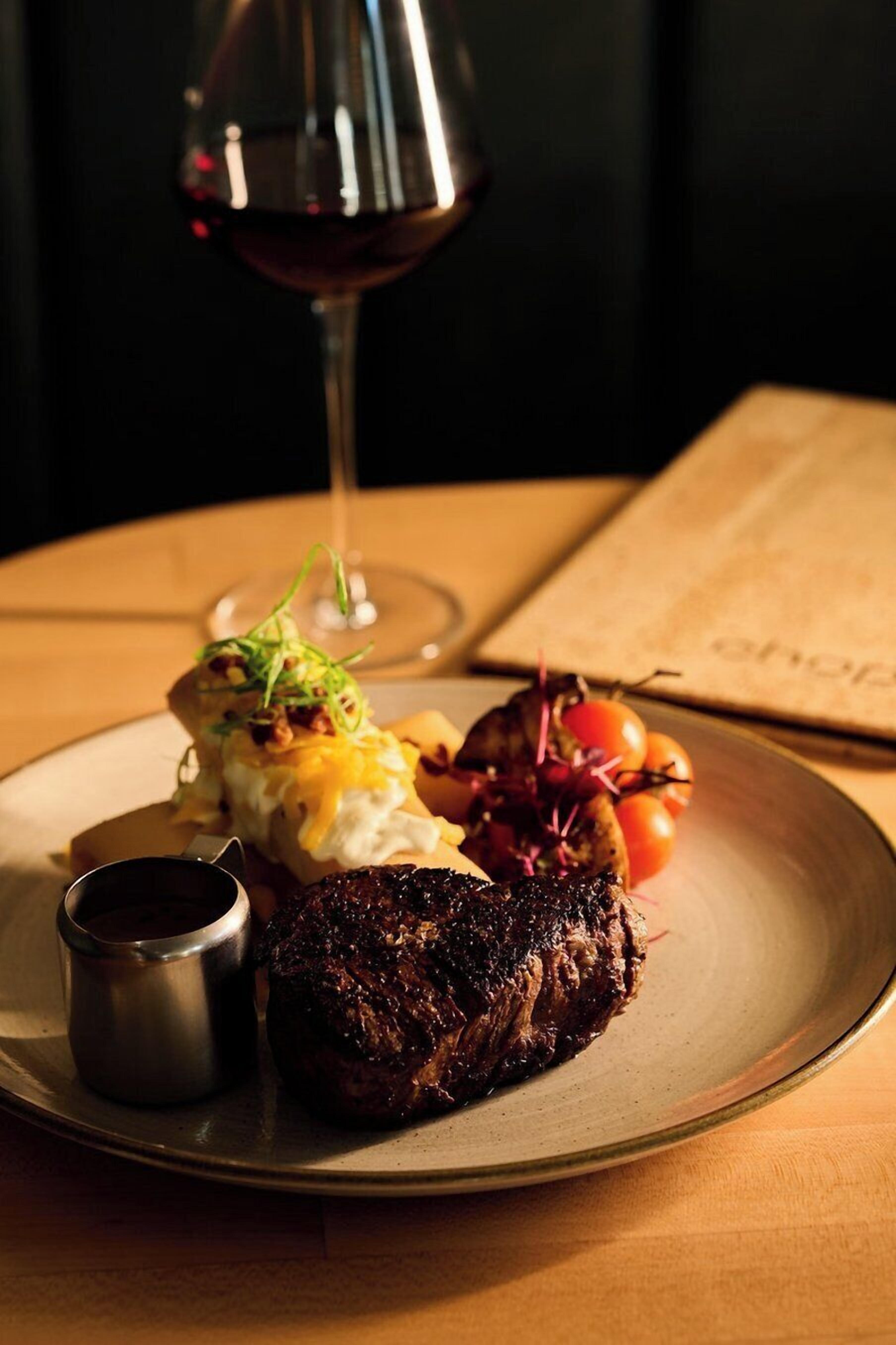 A plate of food with a steak, vegetables, and a glass of red wine on a table.