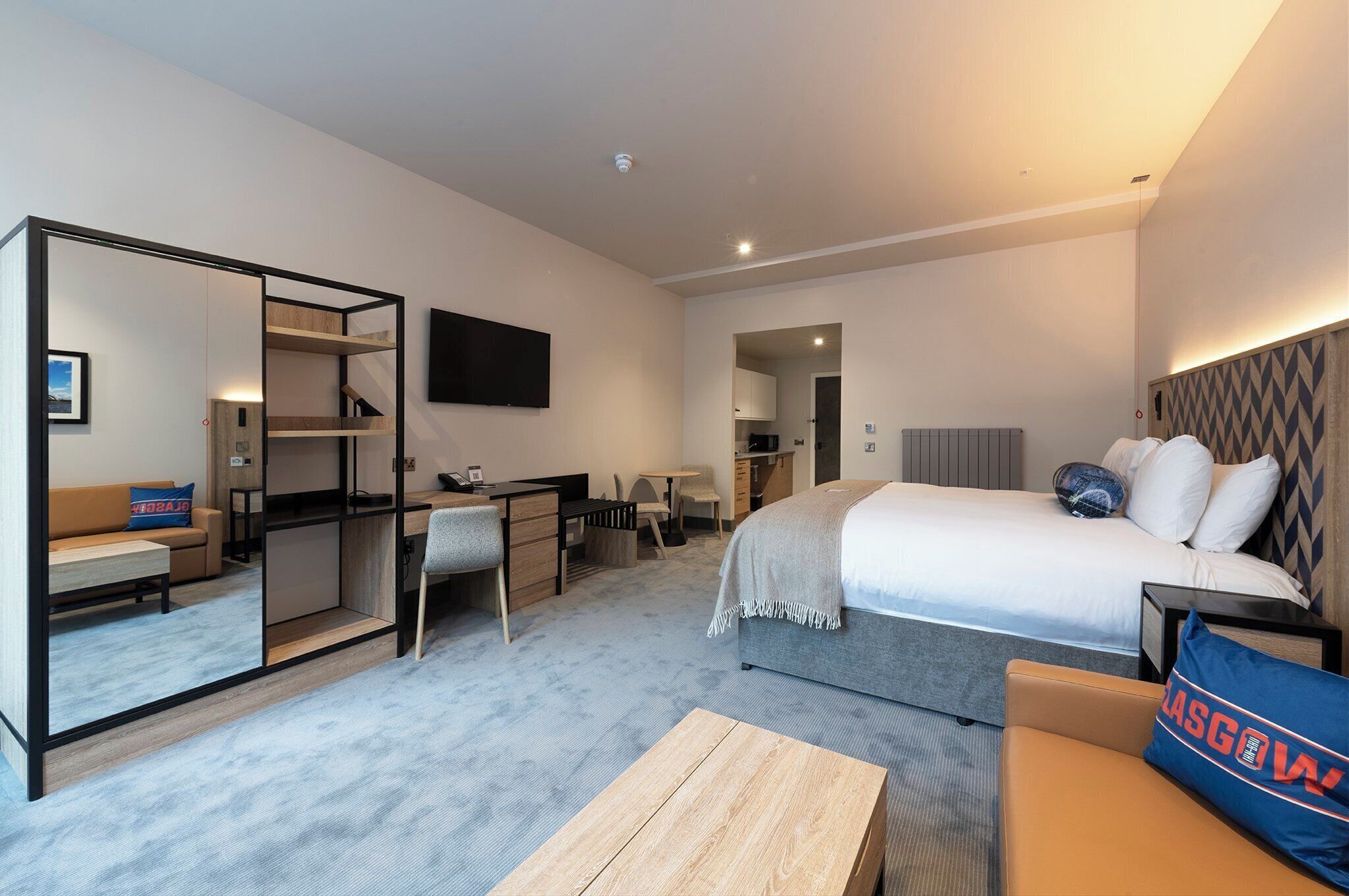 A modern hotel room with a bed, desk, chair, and a sofa.