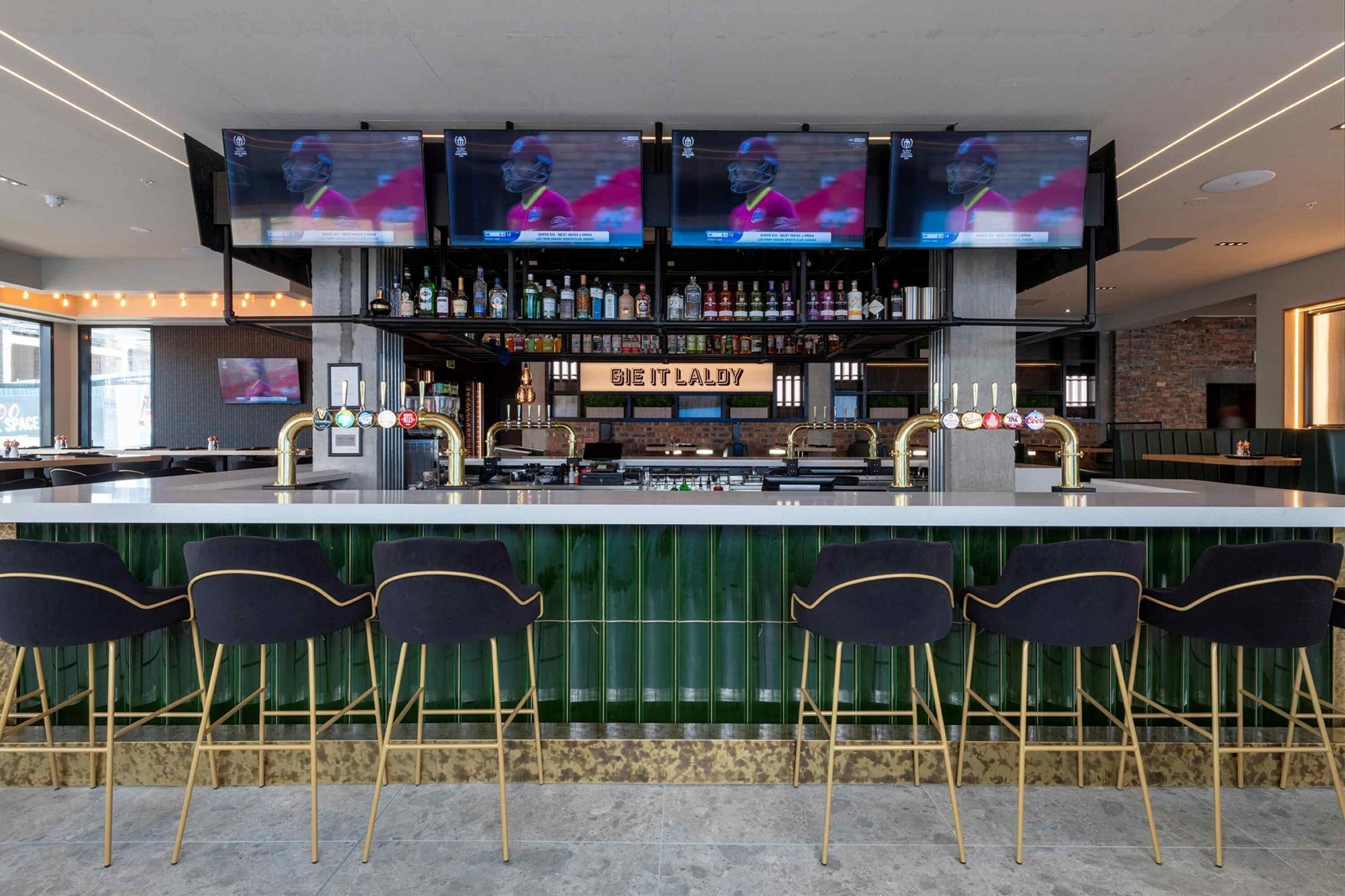 A bar area with multiple TVs, a bar counter, and bar stools.