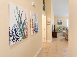 A hallway with artwork on the walls, a door leading to a living area with a sofa and a television. - Bikini Bungalow - King Beds and Short Walk to the Beach! Pet Friendly! (St. Augustine)