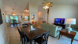 A spacious living area with a dining table, sofa, TV, and ceiling fan. - Bikini Bungalow - King Beds and Short Walk to the Beach! Pet Friendly! (St. Augustine)