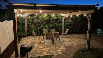 Eine Terrasse im Freien mit einer Holz-Pergola, Backsteinpflaster und Lichterketten.