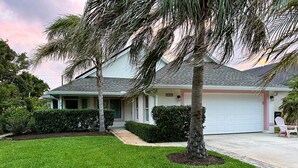 A single-story house with a garage, surrounded by a well-maintained lawn and palm trees. - Bikini Bungalow - King Beds and Short Walk to the Beach! Pet Friendly! (St. Augustine)
