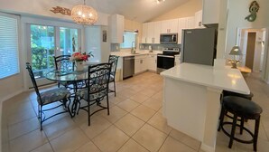 A modern kitchen with white cabinets, a stainless steel refrigerator, a microwave, and an oven. There is a dining area with a glass table and chairs. - Bikini Bungalow - King Beds and Short Walk to the Beach! Pet Friendly! (St. Augustine)