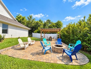 A backyard patio with a fire pit, outdoor seating, and a pergola.