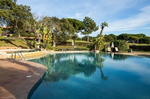 Une piscine bordée d’une terrasse en briques, entourée d’arbres et d’une pelouse bien entretenue.