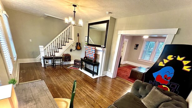 A living room with a wooden floor, a gray sofa, a dining table, and a staircase leading to another level. - Newly Updated: Nearby Short North / OSU! (Columbus)