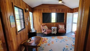 A wooden-paneled room with a dining table, two chairs, a small side table, and a window with blinds.