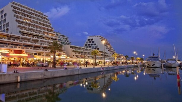Ein Hotel am Wasser mit mehreren Balkonen, einer Marina voller Yachten und einem Spiegelbild im Wasser.