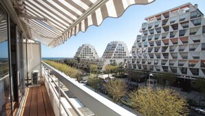 Ein Balkon mit Blick auf moderne Gebäude, einen klaren Himmel und eine entfernte Küstenlinie.