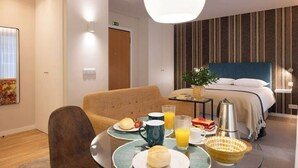 A hotel room with a bed, a dining table with breakfast, a sofa, and a large window. - Wanderlust Apartment, by Bolhão Residences (Porto)