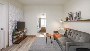 A modern living room with a grey sofa, a TV on a wooden stand, a patterned rug, and a bookshelf. - Golden oak one bedroom w a cool patio for vacation (Austin)