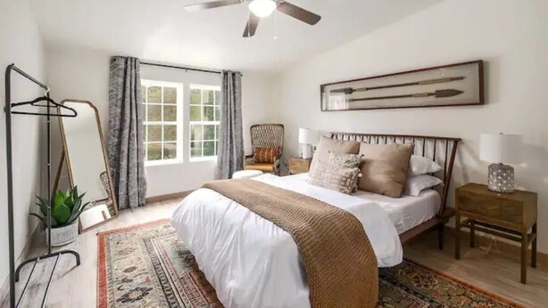 A bedroom with a bed, a ceiling fan, a window with curtains, a bedside table, and a framed picture on the wall. - Golden oak one bedroom w a cool patio for vacation (Austin)